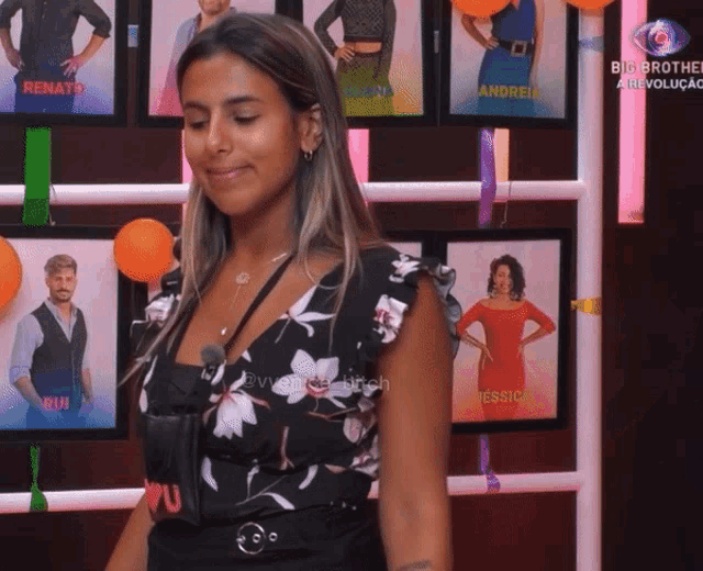 a woman stands in front of a wall with pictures of big brother