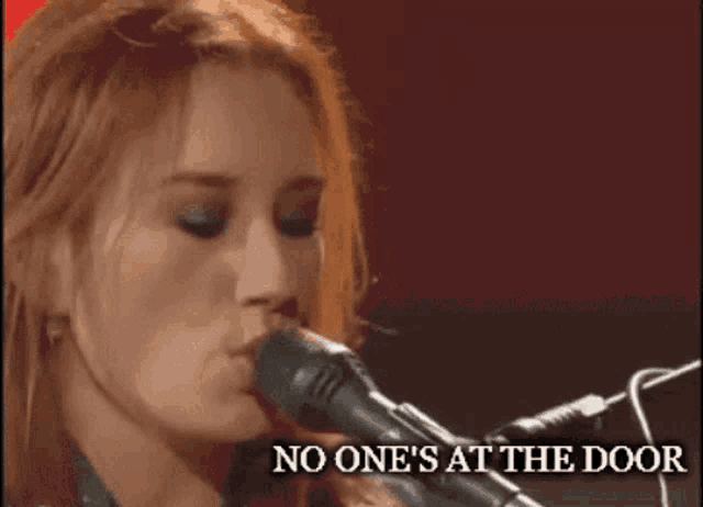a woman singing into a microphone with the words " no one 's at the door " above her