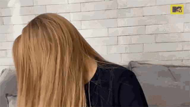 a woman with long blonde hair is sitting on a couch and covering her face with her hair