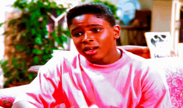 a young man in a pink shirt is sitting in a chair