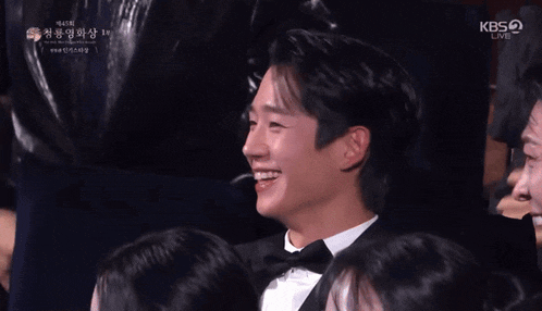 a man in a tuxedo is surrounded by people and the kbs logo can be seen in the corner