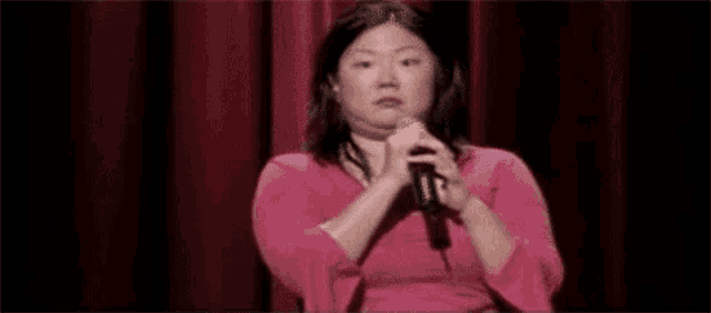 a woman is holding a microphone in front of a red curtain .