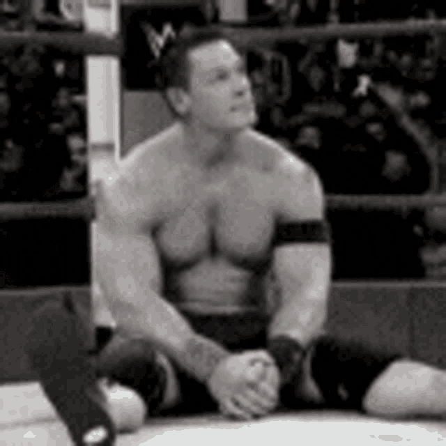 a black and white photo of a shirtless wrestler sitting in a boxing ring .