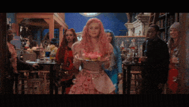 a woman with pink hair is holding a plate of food in her hand