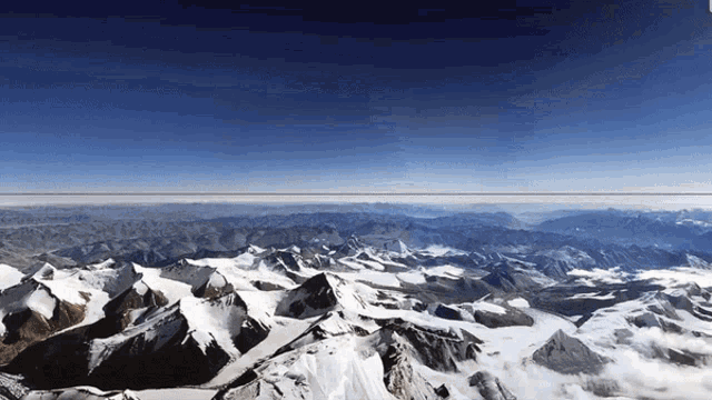 an aerial view of snow covered mountains with a blue sky in the background