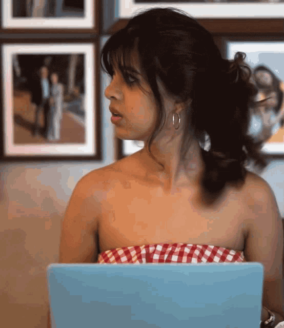 a woman in a red and white checkered top sits in front of a blue laptop