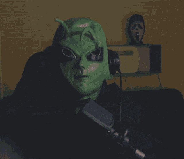 a person wearing a green mask with a scream mask in the background