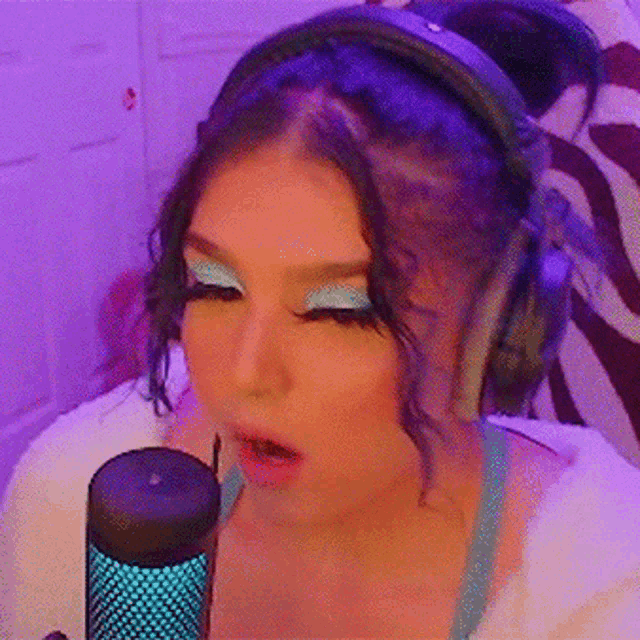 a woman wearing headphones and blue eye shadow sings into a microphone