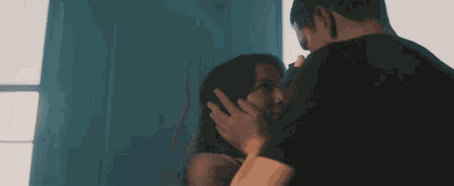a man and woman are touching each other 's faces in front of a window