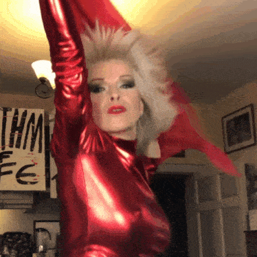 a woman in a red latex outfit is standing in front of a sign that says thm fe