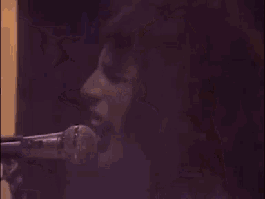 a woman is singing into a microphone in front of a purple wall .