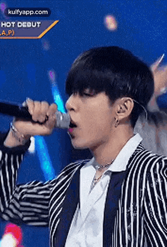 a young man is singing into a microphone on a stage .