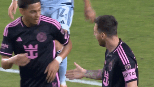 two soccer players are shaking hands on the field and one of them is wearing a shirt that says capital