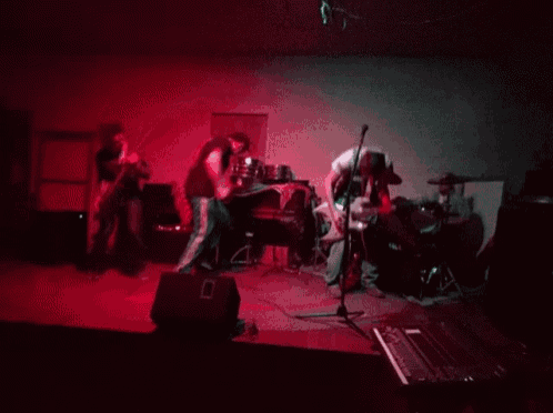 a group of people playing instruments on a stage with red lights behind them