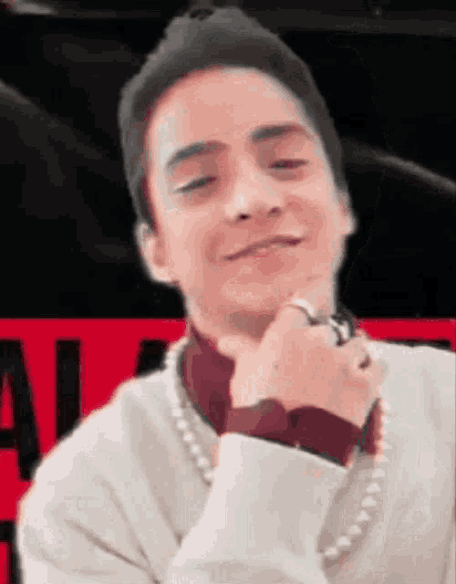 a man wearing a pearl necklace and a ring on his finger is smiling and looking at the camera .
