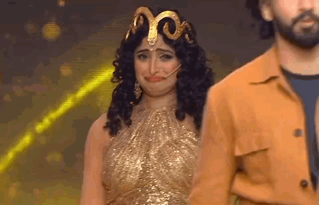 a woman in a gold dress with a crown on her head is crying while standing next to a man .