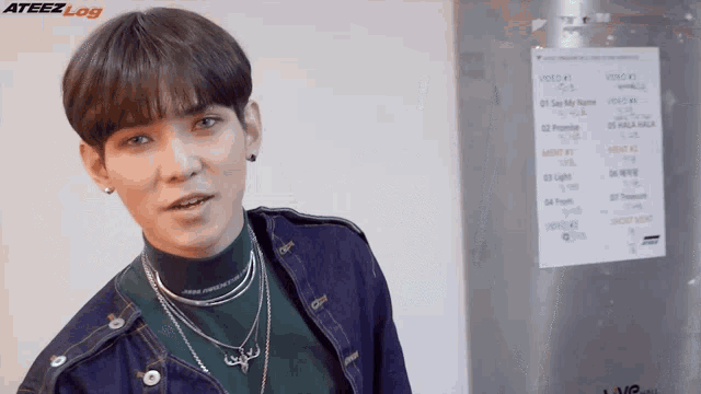 a young man standing in front of a sign that says ateez log