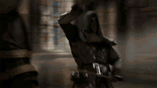 a man in a hooded cloak is holding a sword in his hand .