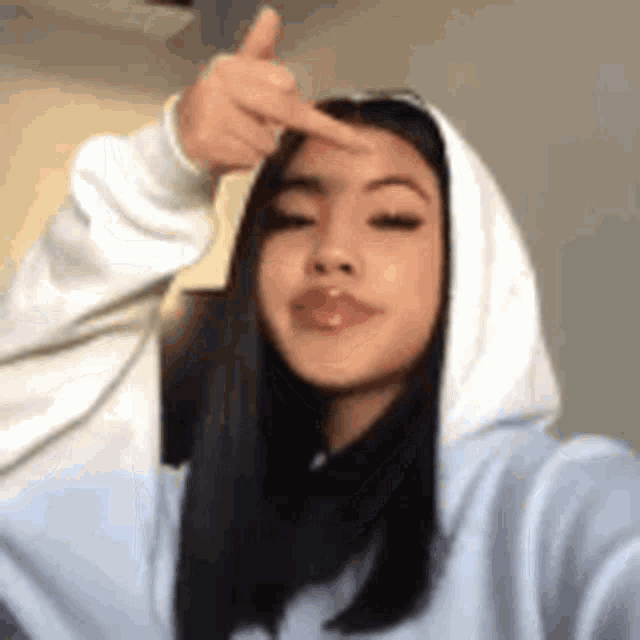 a girl in a hoodie is taking a selfie and making a funny face .