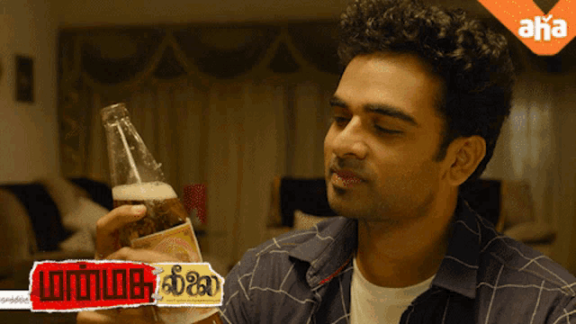 a man is holding a bottle of beer in front of a sign that says aaha