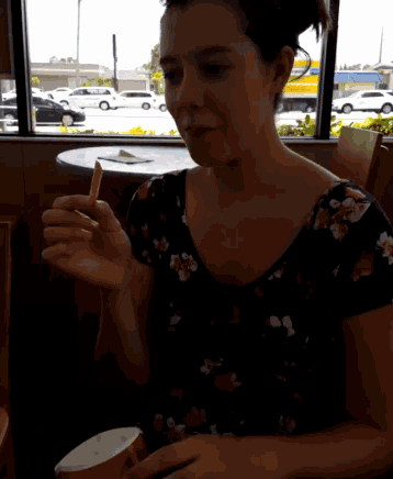 a woman eating french fries in front of a window with a yellow truck in the background