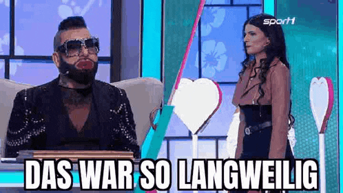 a man with a beard and sunglasses is sitting next to a woman in a dress on a television show .