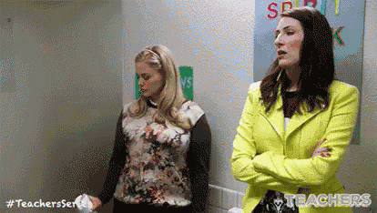 two women are standing in a bathroom with their arms crossed . one of the women is wearing a neon yellow jacket .
