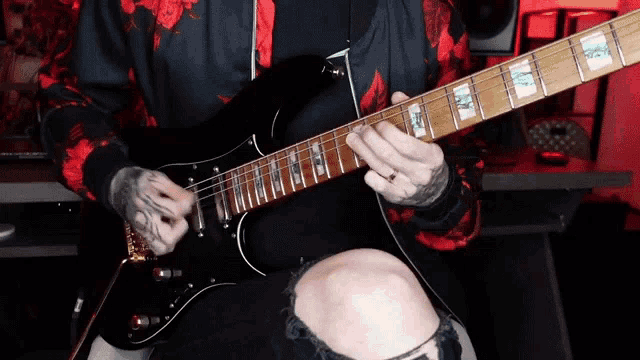 a man in a red and black hoodie is playing an electric guitar .