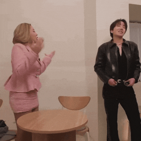 a woman in a pink suit stands next to a man in a black leather jacket