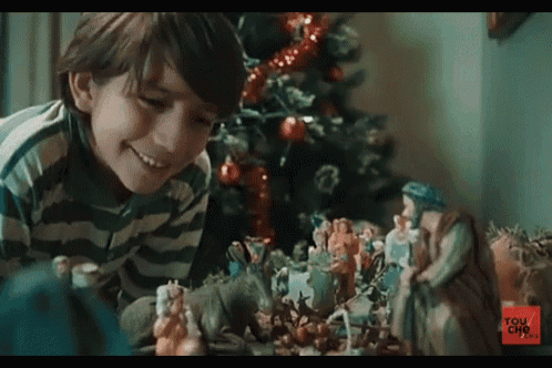 a young boy is playing with a nativity scene in front of a christmas tree sponsored by tou cho