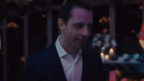 a close up of a man 's face in a dark room with purple lights behind him .