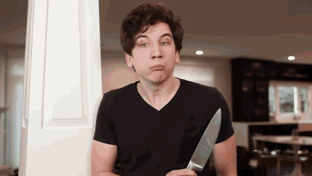 a man in a black shirt is holding a large knife and making a funny face
