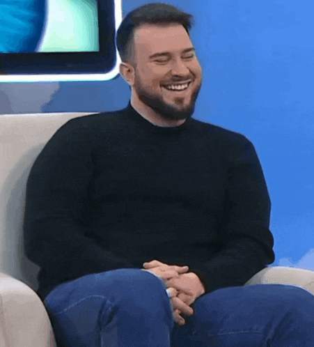 a man with a beard is smiling while sitting in a chair with his eyes closed
