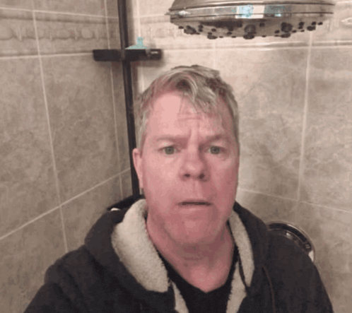 a man taking a selfie in a bathroom with a shower head above him