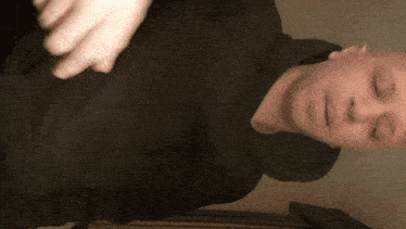 a man wearing a black hoodie with his eyes closed looks at the camera
