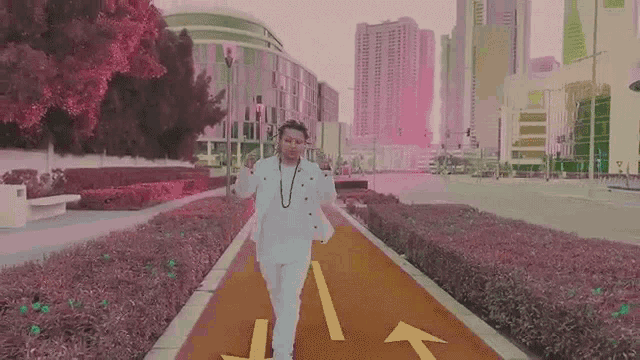 a man in a white suit is walking down a green path in a park .