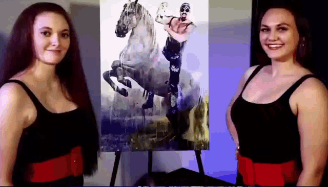 two women are standing in front of a painting of a man riding a horse