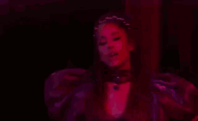 ariana grande is wearing a purple dress and a choker while singing into a microphone in a pink room .