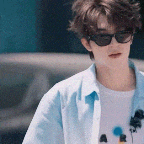 a young man wearing sunglasses and a blue shirt is walking down a street .