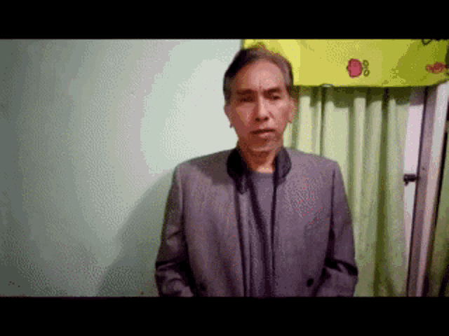 a man in a suit stands in front of a green curtain and a yellow sign that says d8