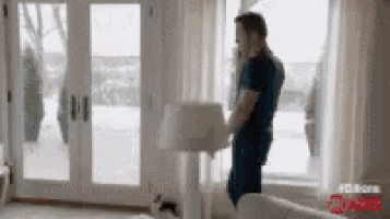 a man is standing in a living room with a lamp and talking on a cell phone .