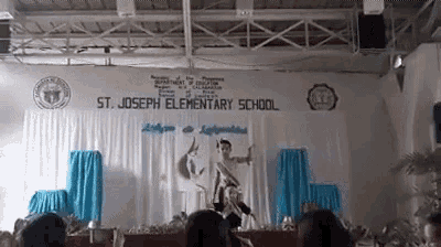 a group of people are sitting in front of a stage with a sign that says st. joseph elementary school .