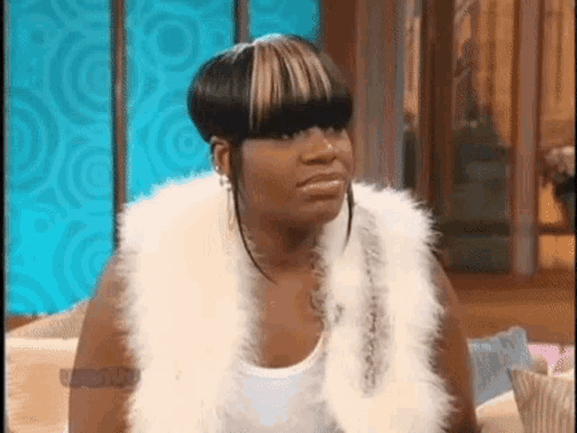 a woman is sitting on a couch wearing a fur vest and making a funny face .