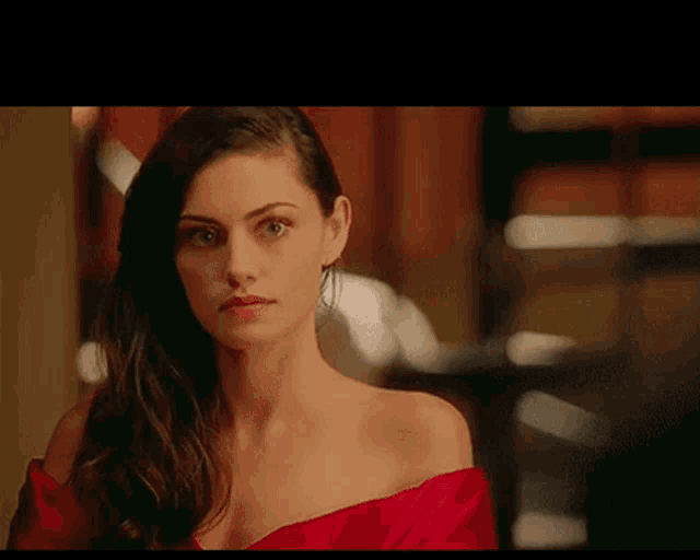 a woman wearing a red off the shoulder top looks at the camera