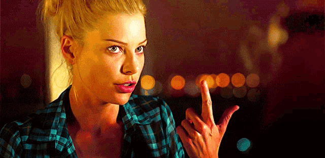 a blonde woman in a plaid shirt is pointing her finger