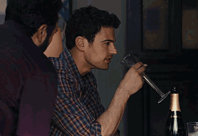 a man in a plaid shirt is drinking from a glass next to a bottle of wine