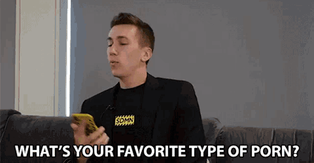 a man is sitting on a couch holding a cell phone and asking what 's your favorite type of porn ?