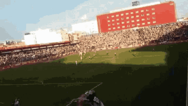 a soccer game is being played in a stadium with a red building in the background