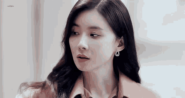 a close up of a woman 's face wearing earrings and a pink coat .