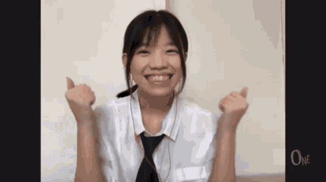 a young girl in a white shirt and tie is smiling and making a fist with her hands .